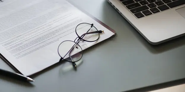 glasses, clipboard, and laptop on table