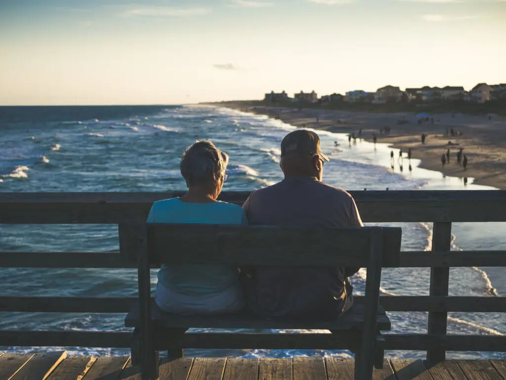 old couple sitting on bench looking into ocean