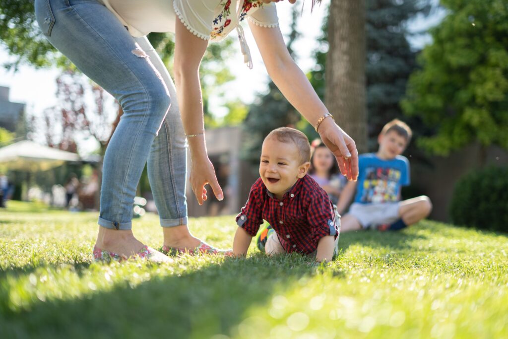 children playing in grass with mother about to pick up a child