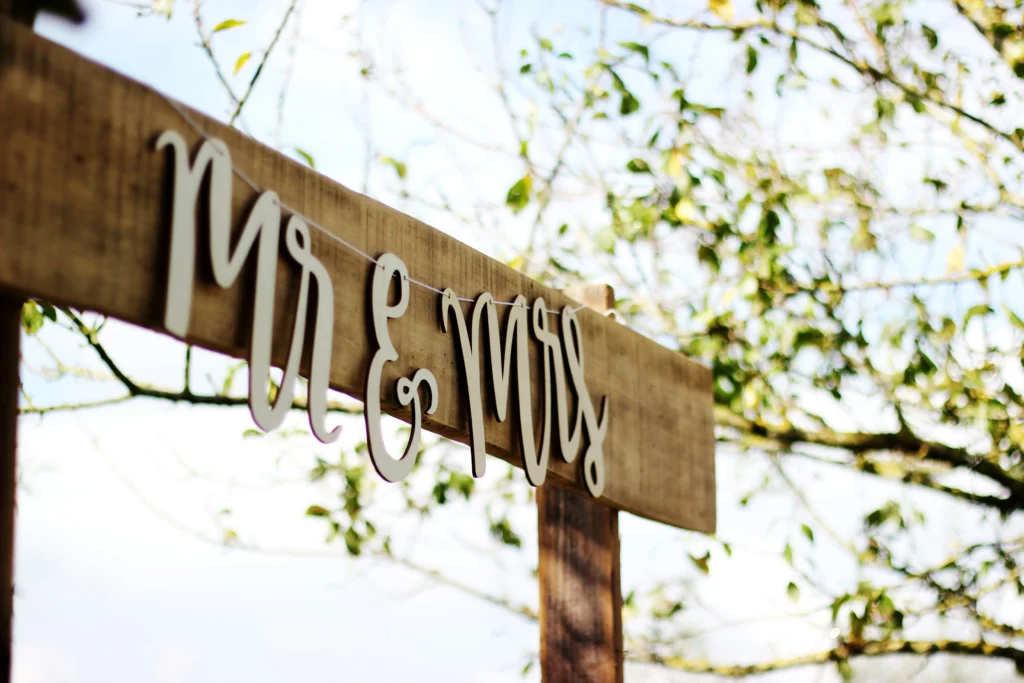 DIY wedding decor. A ”Mr. & Mrs.” sign is on some sting, hanging off a plank of wood. It’s a DIY wedding decoration at an outdoor wedding.