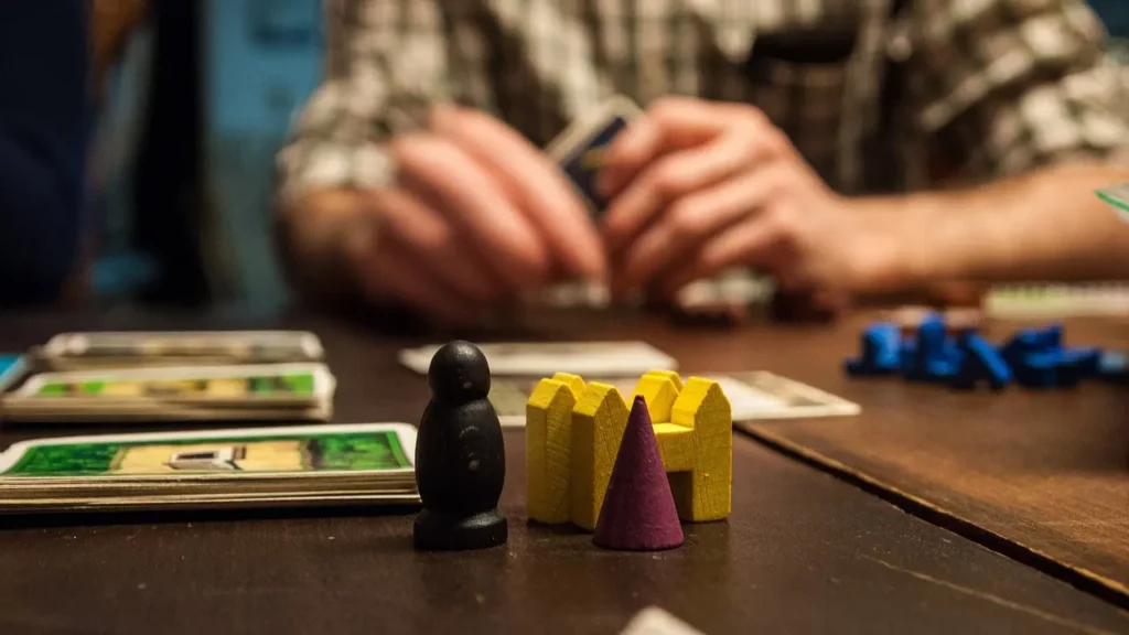 Game pieces red on a table along with cards as a person sits across. Friends and family enjoy playing 4th of July games to celebrate the holiday.
