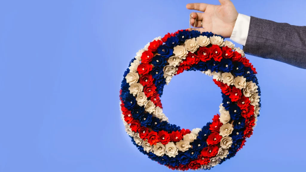 Festive 4th of July decor. A hand holding a wreath made up of red, white, and blue flowers.