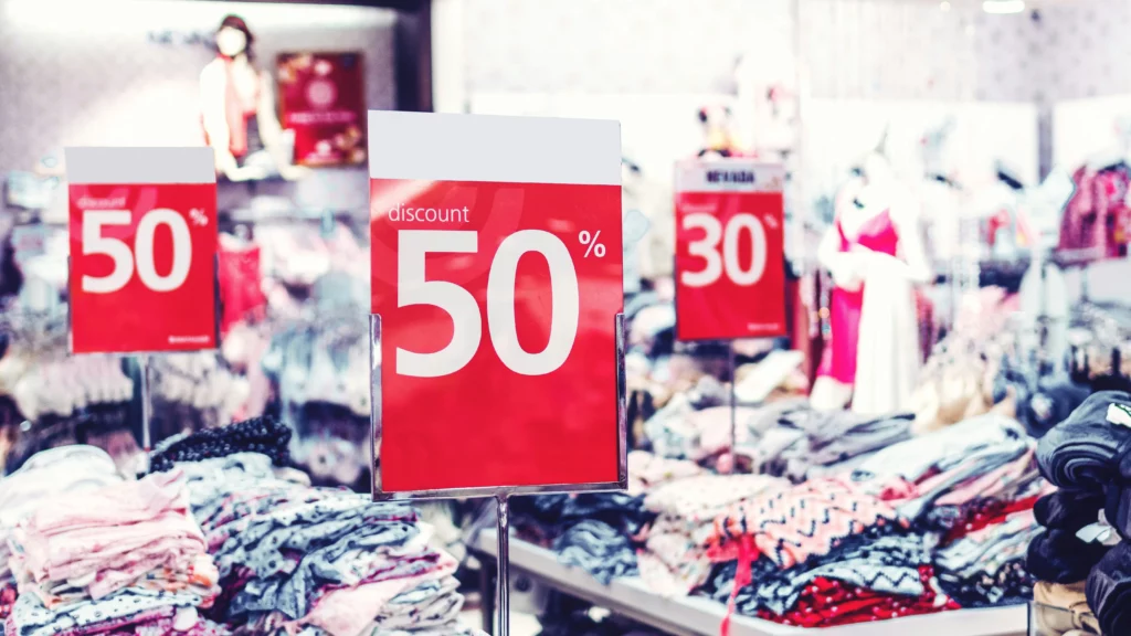 A shop with sales and a clearance section. Piles of clothing with large signs displaying 50% and 30% discounts.
