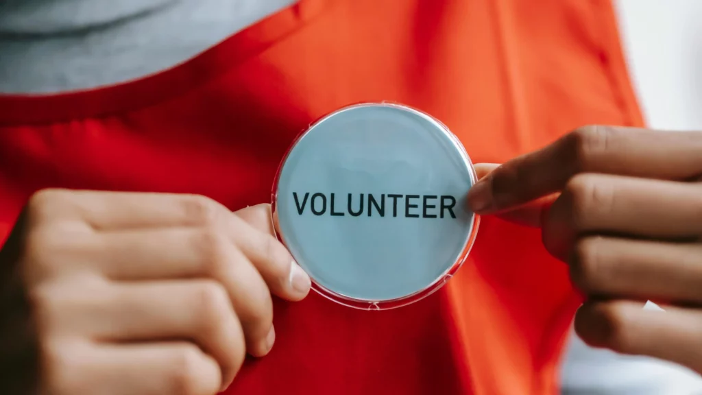 Two hands holding a white badge that says volunteer in black text.