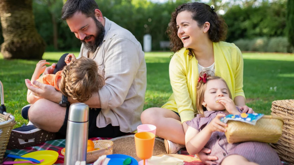 Two adults and two young children having a picnic outdoors.