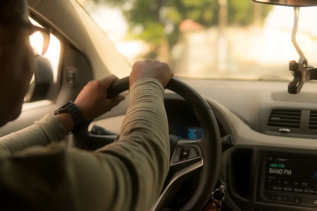 View of a driver working a car service side hustle. They are wearing glasses and having both hands on the steering wheel.