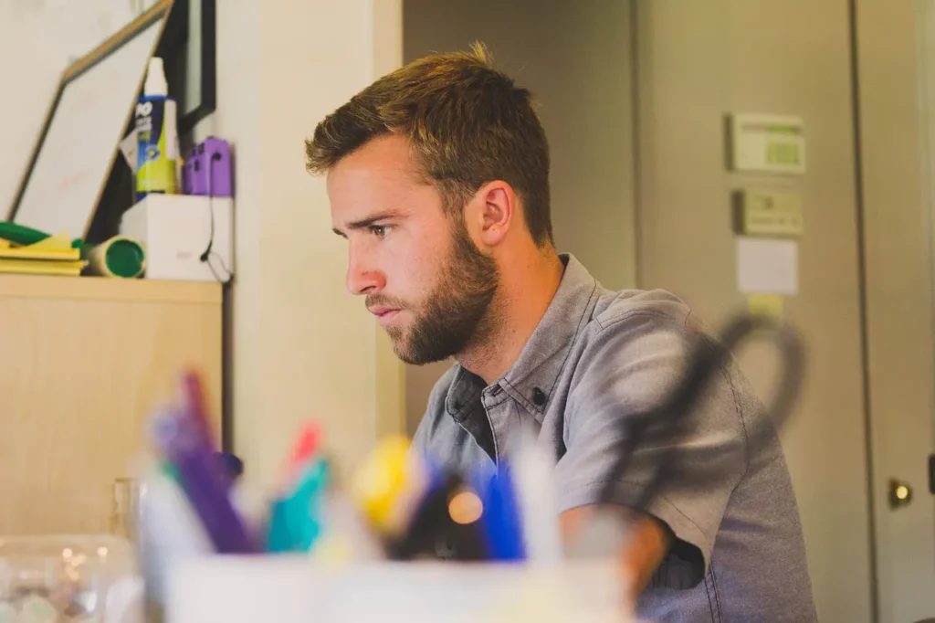 A small business owner is looking at something white. The shot is captured with an assortment of pens, markers, highlighters, and a pair of scissors in a holder in front.