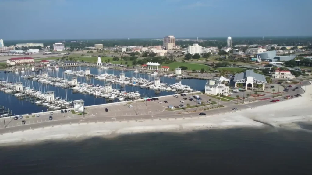 Snapshot of the Mississippi Gulfport beach with rows of boats parked next to one another while there is a parking lot with cars in front of it. Several buildings and other structures are seen scattered throughout the land.