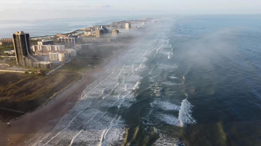 Snapshot of the Texas South Padre Island beach meeting dark choppy waters. Several buildings are seen along the beach.