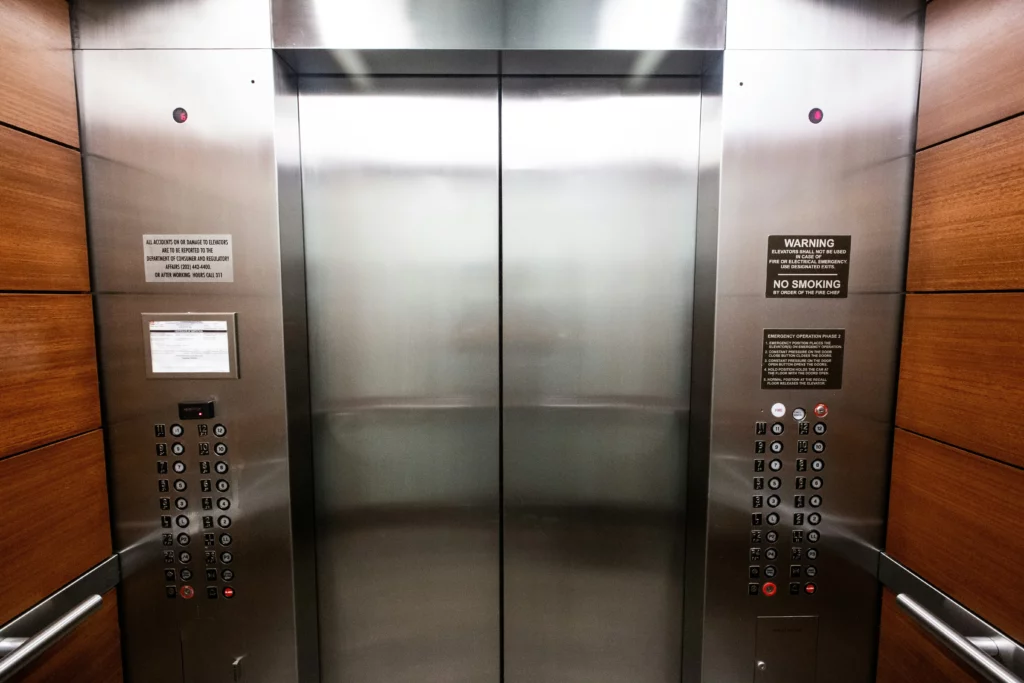Image of closed elevators door captured from inside the elevator with several buttons along both sides of it.