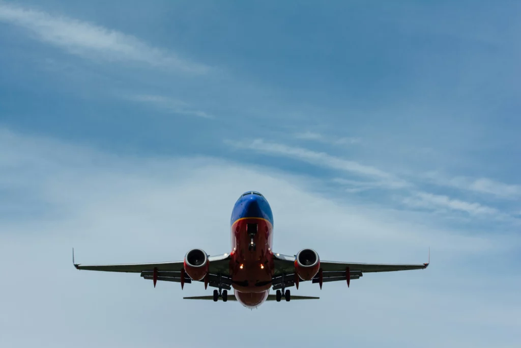 Front and partial bottom view of an airplane captured against a blue sky with some clouds